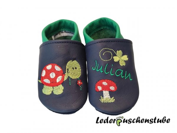 Lederpuschen dunkelblau-ital.grün  mit rechts Stickerei Schild Blume (rot-creme-hellgrün-schwarz) Blume (rot-creme) und links Namen (ital.grün), Kleeblatt (hellgrün) und Pilz schlicht (rot-weiß-creme-hellgrün)